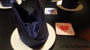 A folded blue cloth napkin on a plate and blue or pink coasters at each place.