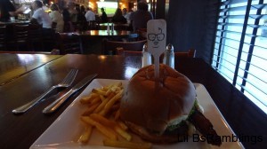 A burger and fries in a bar with a stick in the burger. The stick has a face on it.