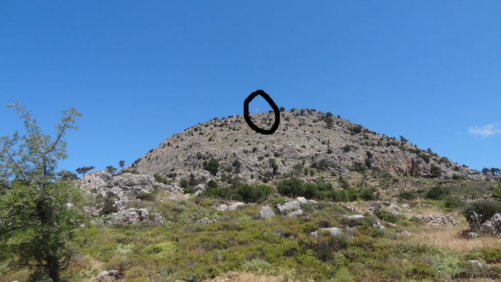 A black circle emphazes a barely visible white cross peeking over a rocky hill.