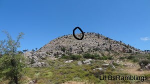 A black circle emphazes a barely visible white cross peeking over a rocky hill.