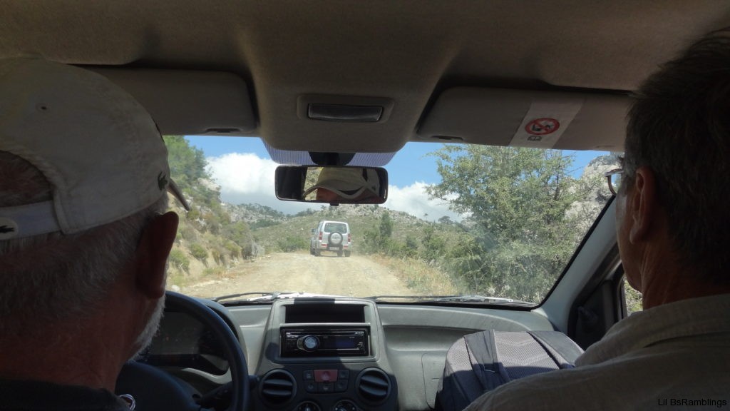A picture through a windshield of a SUV driving winding mountain roads taken between the driver and passenger of the car.