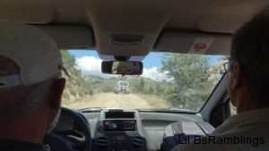 A picture through a windshield of a SUV driving winding mountain roads taken between the driver and passenger of the car.